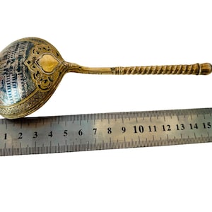 Op de afbeelding: Een zilveren en gouden lepel met een sierlijk ontwerp en een gedraaide steel. De lepel is ongeveer 18 cm lang.