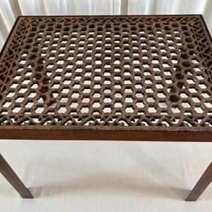 May include: A square table featuring a dark brown, rusted metal frame and a flat top surface with an intricate, openwork geometric lattice pattern. The table is supported by four straight, slender metal legs, showcasing a weathered, textured finish.