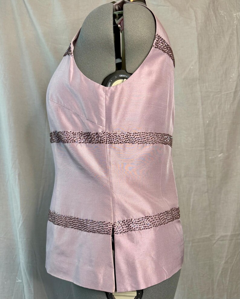 May include: Pale pink sleeveless top with a V-neckline. The top is embellished with rows of dark brown beading. The fabric has a subtle sheen. The garment is displayed on a mannequin.