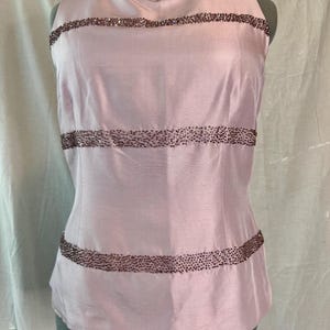 May include: A sleeveless, pale pink top with horizontal bands of small, dark beads. The top is made of a smooth, possibly silk-like fabric and has a fitted silhouette. The beaded bands add a touch of sparkle and detail to the garment.
