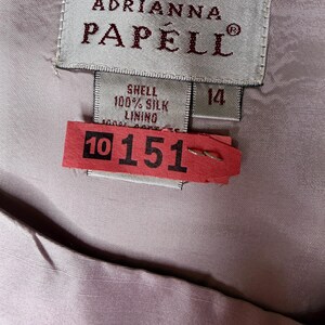 May include: Close-up of a label from Adrianna Papell, size 14. The label reads "Shell 100% Silk Lining". A red tag with the numbers "10 151" is attached to the garment.
