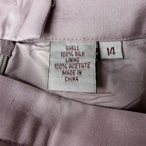 May include: Close-up of a light purple garment with a label indicating it's made of 100% silk shell and 100% acetate lining. The label also states "Made in China" and the size is 14.
