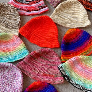 May include: A collection of 12 crocheted hats in various colors and patterns, including rainbow, pink, orange, blue, and white.