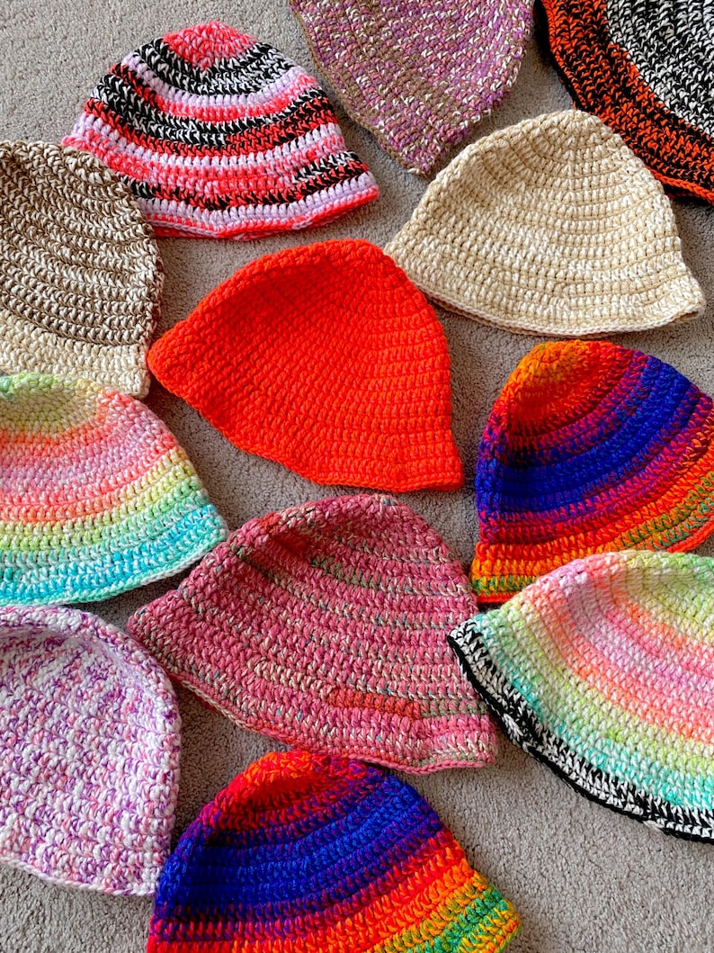 May include: A collection of 12 crocheted hats in various colors and patterns, including rainbow, pink, orange, blue, and white.