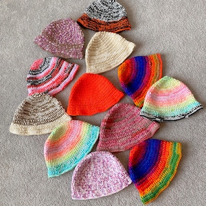 May include: A collection of 12 crocheted bucket hats in various colors and patterns, including rainbow, pink, orange, and brown.