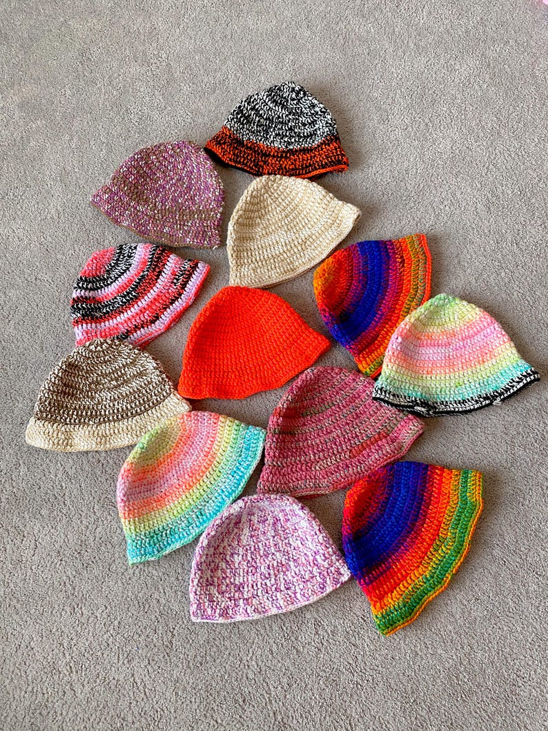 May include: A collection of 12 crocheted bucket hats in various colors and patterns, including rainbow, pink, orange, and brown.