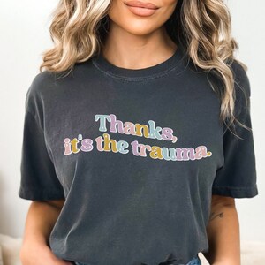 May include: A dark gray t-shirt with the text "Thanks, it's the trauma." in rainbow colors.