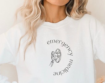 May include: White long-sleeved sweatshirt with the words "emergency medicine" in a circular design, and a medical symbol in the center. The word "white" is printed at the bottom left.