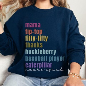 May include: Navy blue sweatshirt with a colourful graphic print that reads "mama tip-top fifty-fifty thanks huckleberry baseball player caterpillar neuro squad".