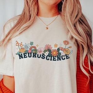 May include: A white t-shirt featuring a colourful floral design and the text "NEUROSCIENCE" in blue lettering.