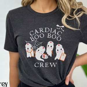 May include: Dark grey heather t-shirt with a graphic of ghosts wearing nurse hats and the text "Cardiac Boo Boo Crew".