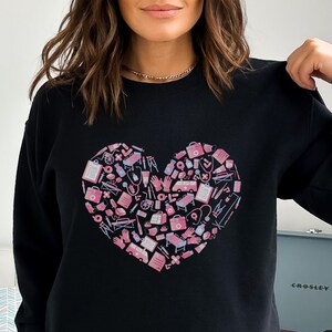 May include: Black sweatshirt with a pink heart design. The heart is filled with medical symbols and icons.