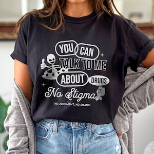 Peut inclure: T-shirt noir avec un graphique blanc d'un extraterrestre dans une soucoupe volante. Le texte sur le t-shirt est "You can talk to me about drugs. No stigma. No judgment. No shame."