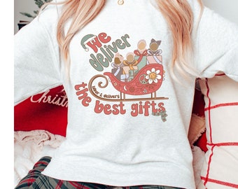 May include: A white sweatshirt with a red and green illustration of a sleigh with three people in it. The text "We deliver the best gifts" is printed on the sweatshirt.