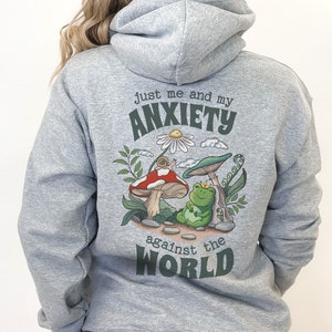 May include: Gray hooded sweatshirt with a green, red, and white graphic of a frog sitting on a mushroom with the text "Just me and my anxiety against the world".