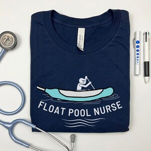 May include: A navy blue t-shirt with a white graphic of a person paddling a blue canoe. The text "FLOAT POOL NURSE" is printed in white below the graphic.