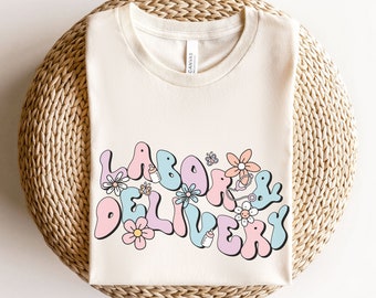 Könnte beinhalten: Ein naturfarbenes T-Shirt mit einem grafischen Design, das "Labor & Delivery" im Retro-Stil mit Blumen und einer Babyflasche zeigt.
