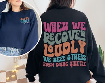May include: Black sweatshirt with the text "When we recover loudly we keep others from dying quietly" in colourful retro font.