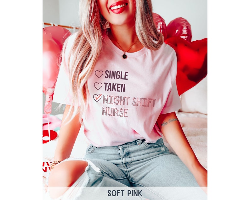 May include: A pink t-shirt with the text "Single, Taken, Night Shift Nurse" with a checkmark next to the last option. The shirt is worn by a person with blonde hair and blue jeans.