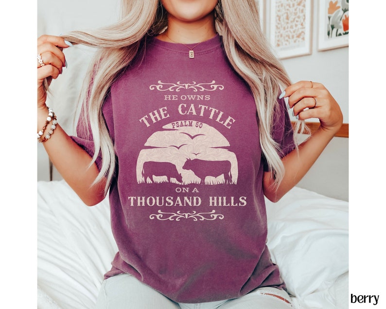 May include: A purple t-shirt with a graphic design that says "He owns the cattle on a thousand hills, Psalm 50". The graphic also includes a silhouette of two cows.