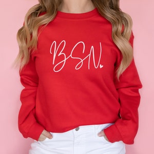 May include: Red sweatshirt with white cursive text that says "BSN" with a small heart after the N.
