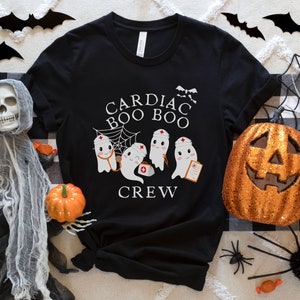 May include: Black t-shirt with a white graphic of three ghosts wearing nurse hats and holding medical equipment. The text "Cardiac Boo Boo Crew" is printed on the shirt.
