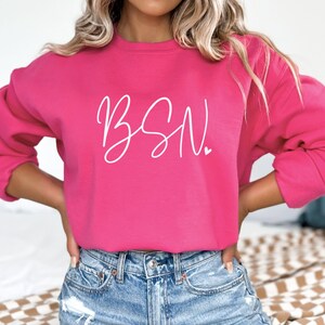 May include: A pink sweatshirt with the text "BSN" in white cursive lettering.