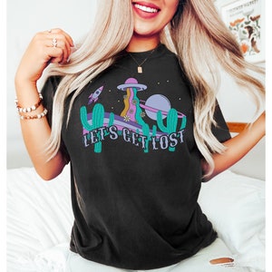 May include: Black t-shirt with a colourful graphic design. The design features a retro-style illustration of a spaceship, planet, cactus, and the text "LET'S GET LOST". The shirt is a comfortable, casual style.