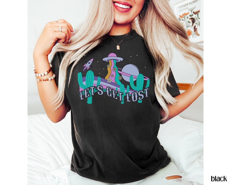 May include: Black t-shirt with a colourful graphic design. The design features a retro-style illustration of a spaceship, planet, cactus, and the text "LET'S GET LOST". The shirt is a comfortable, casual style.