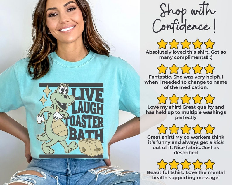 May include: A light blue t-shirt with a cartoon dinosaur graphic and the words "LIVE LAUGH TOASTER BATH". The dinosaur is green and beige, and the toaster is beige. The shirt also has customer reviews.