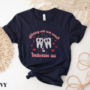 Puede incluir: Camiseta azul marino con un gr&aacute;fico de dos dientes de dibujos animados con corazones y el texto "Nada se interpondr&aacute; jam&aacute;s entre nosotros".
