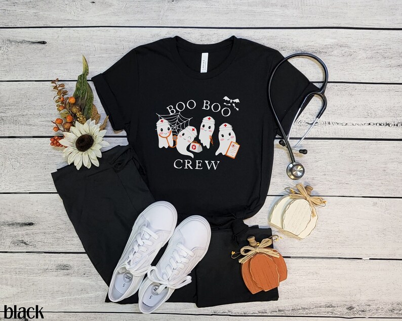 May include: Black t-shirt with a white graphic of ghosts dressed as nurses. The text "BOO BOO CREW" is printed on the shirt.