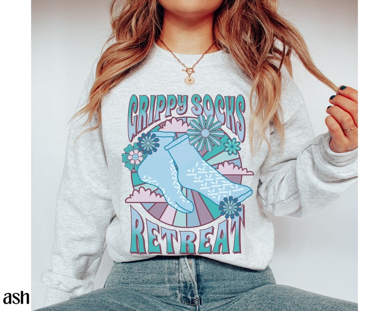 May include: A light gray sweatshirt with a graphic design of blue socks with a white pattern and the text "Grippy Socks Retreat" in a retro font.