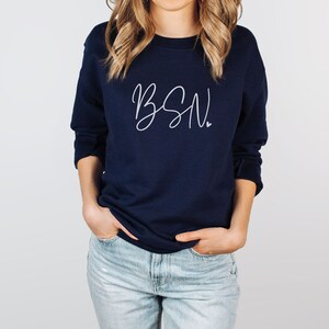 May include: A navy blue sweatshirt with the text "BSN" in white script lettering. The sweatshirt has a crew neck and long sleeves.