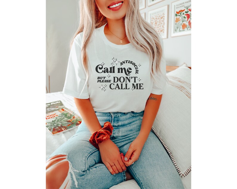 Puede incluir: Camiseta blanca con texto negro que dice "Antisocial Call Me But Please Don't Call Me". El texto est&aacute; en un estilo de fuente retro y est&aacute; rodeado de peque&ntilde;as estrellas.