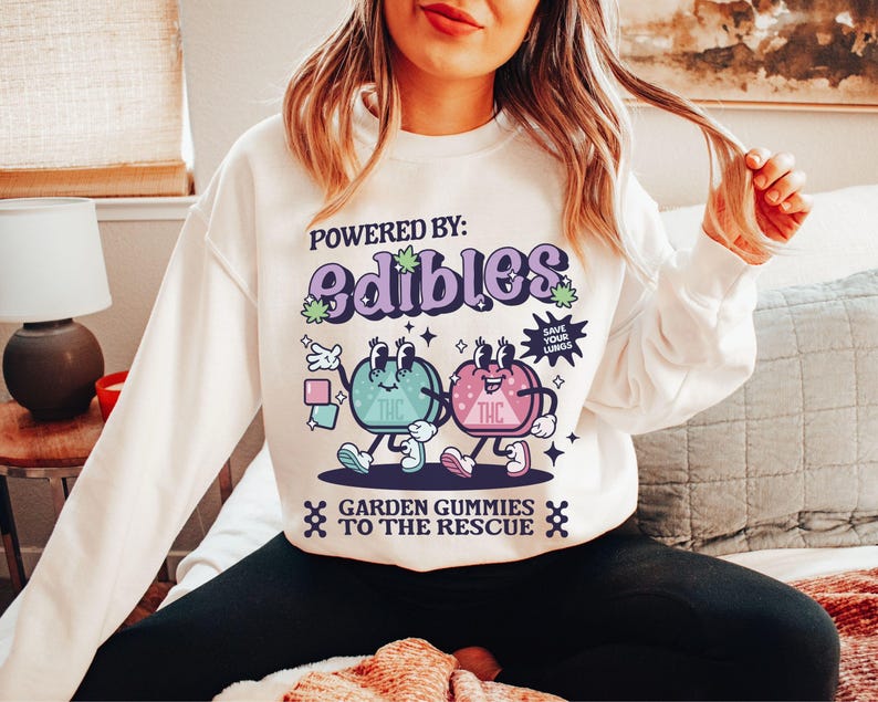 May include: White sweatshirt with a graphic of two cartoon gummies with the text "Powered by: Edibles" and "Garden Gummies to the Rescue".
