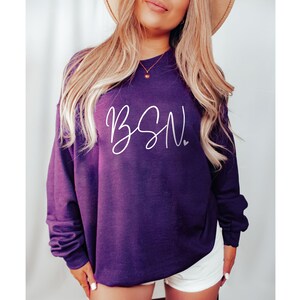 May include: A purple sweatshirt with the text "BSN" in white script lettering and a small white heart.