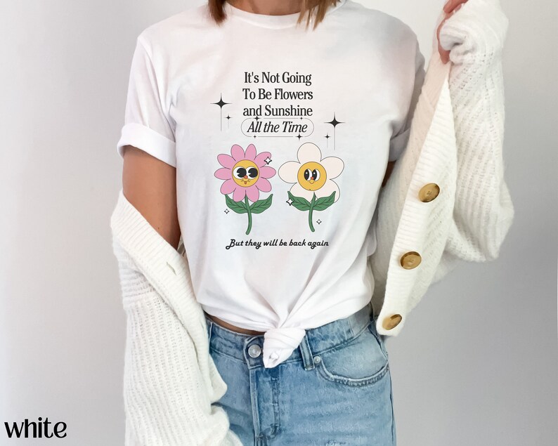 May include: White t-shirt with a graphic of two cartoon flowers with faces. The text on the shirt reads "It's Not Going To Be Flowers and Sunshine All the Time. But they will be back again."