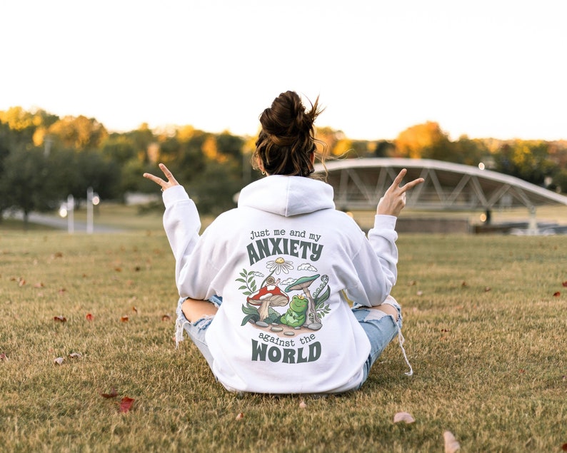 May include: White hoodie with a green, red, and yellow mushroom graphic and the text "Just me and my anxiety against the world".