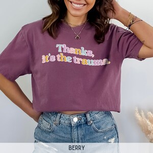 May include: A mauve cropped t-shirt with the text "Thanks, it's the trauma." in colorful letters.