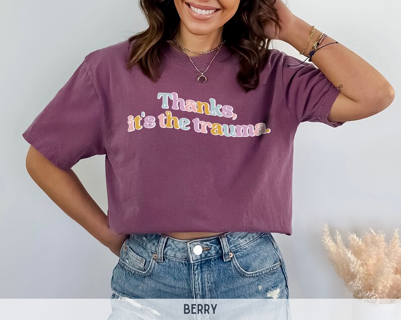 May include: A mauve cropped t-shirt with the text "Thanks, it's the trauma." in colorful letters.