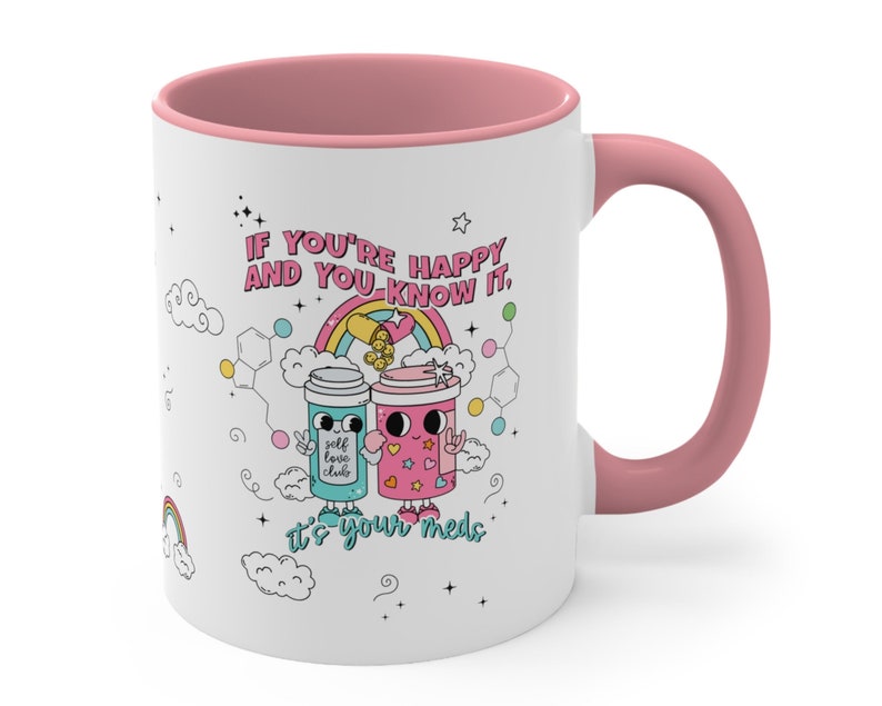 May include: White ceramic mug with a pink rim and handle. The mug features a colourful illustration of two cartoon coffee cups with the text "IF YOU'RE HAPPY AND YOU KNOW IT. It's your meds."