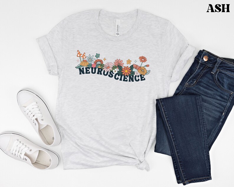 May include: A light grey t-shirt with a graphic design of flowers and mushrooms. The text "NEUROSCIENCE" is printed in dark blue letters.