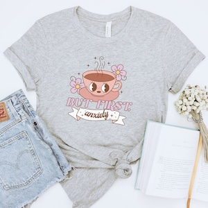 May include: Gray t-shirt with a pink and white cartoon coffee cup with the text "BUT FIRST, anxiety" on a white banner.