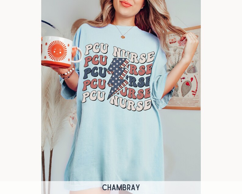 K&ouml;nnte beinhalten: Hellblaues T-Shirt mit einem Grafikdruck eines rot-wei&szlig;-blauen Blitzes und dem Text "PCU NURSE", der in einer Retro-Schrift wiederholt wird.