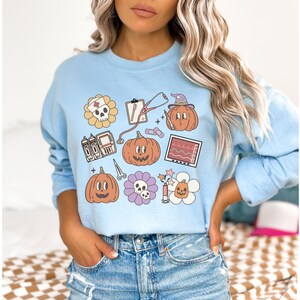May include: Light blue sweatshirt with a graphic print of various Halloween-themed medical symbols, including pumpkins, a stethoscope, a skull, and a heart monitor.