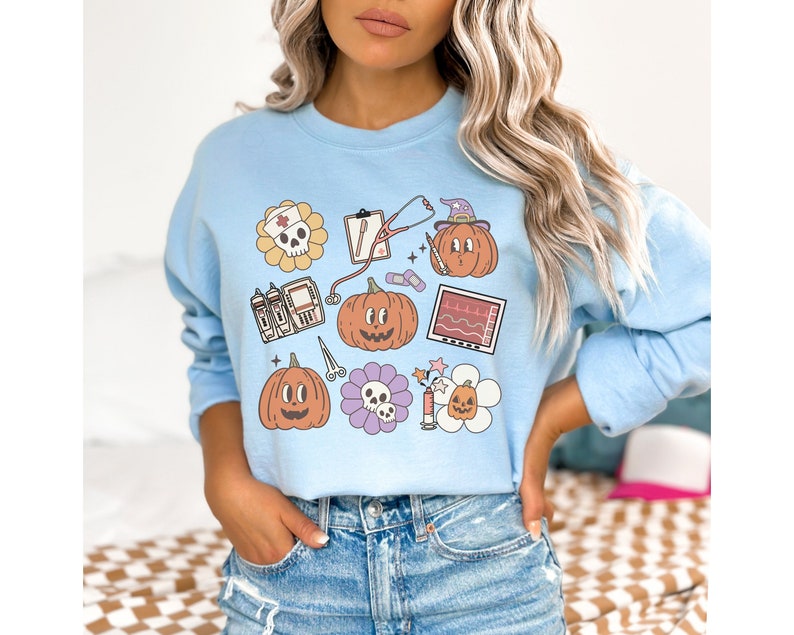 May include: Light blue sweatshirt with a graphic print of various Halloween-themed medical symbols, including pumpkins, a stethoscope, a skull, and a heart monitor.