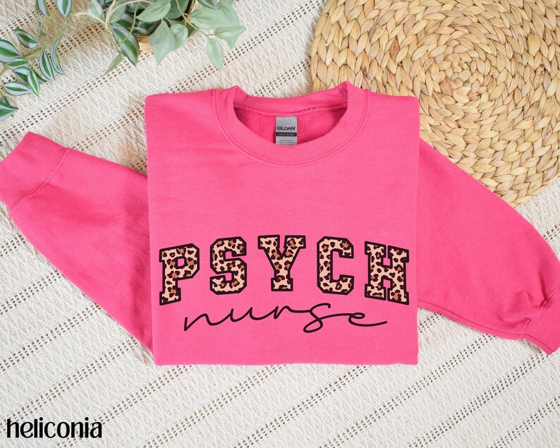 May include: A bright pink sweatshirt with the words "PSYCH nurse" printed on the front. The word "PSYCH" is in a bold, block letter style with a leopard print pattern. The word "nurse" is in a cursive font.