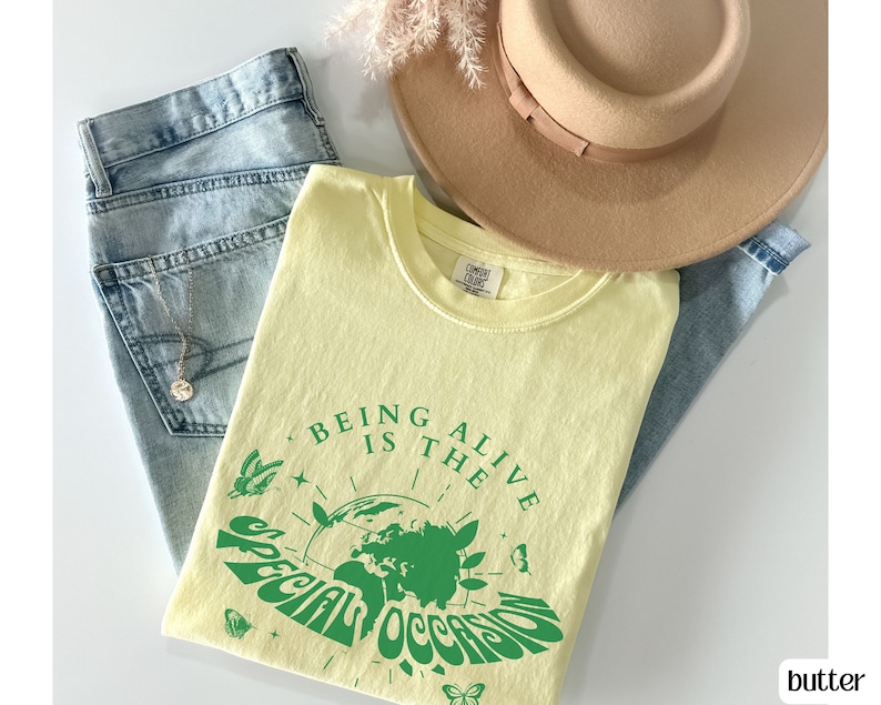 May include: A yellow t-shirt with a green graphic that says "Being alive is the special occasion". The graphic features a globe with butterflies and stars around it.