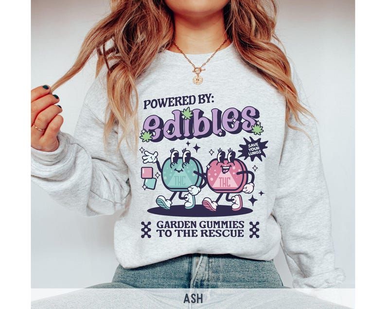 May include: A gray sweatshirt with a graphic of two cartoon gummies. The gummies are green and pink and have the word "THC" on them. The text on the sweatshirt reads "Powered by: edibles Save your lungs Garden gummies to the rescue".
